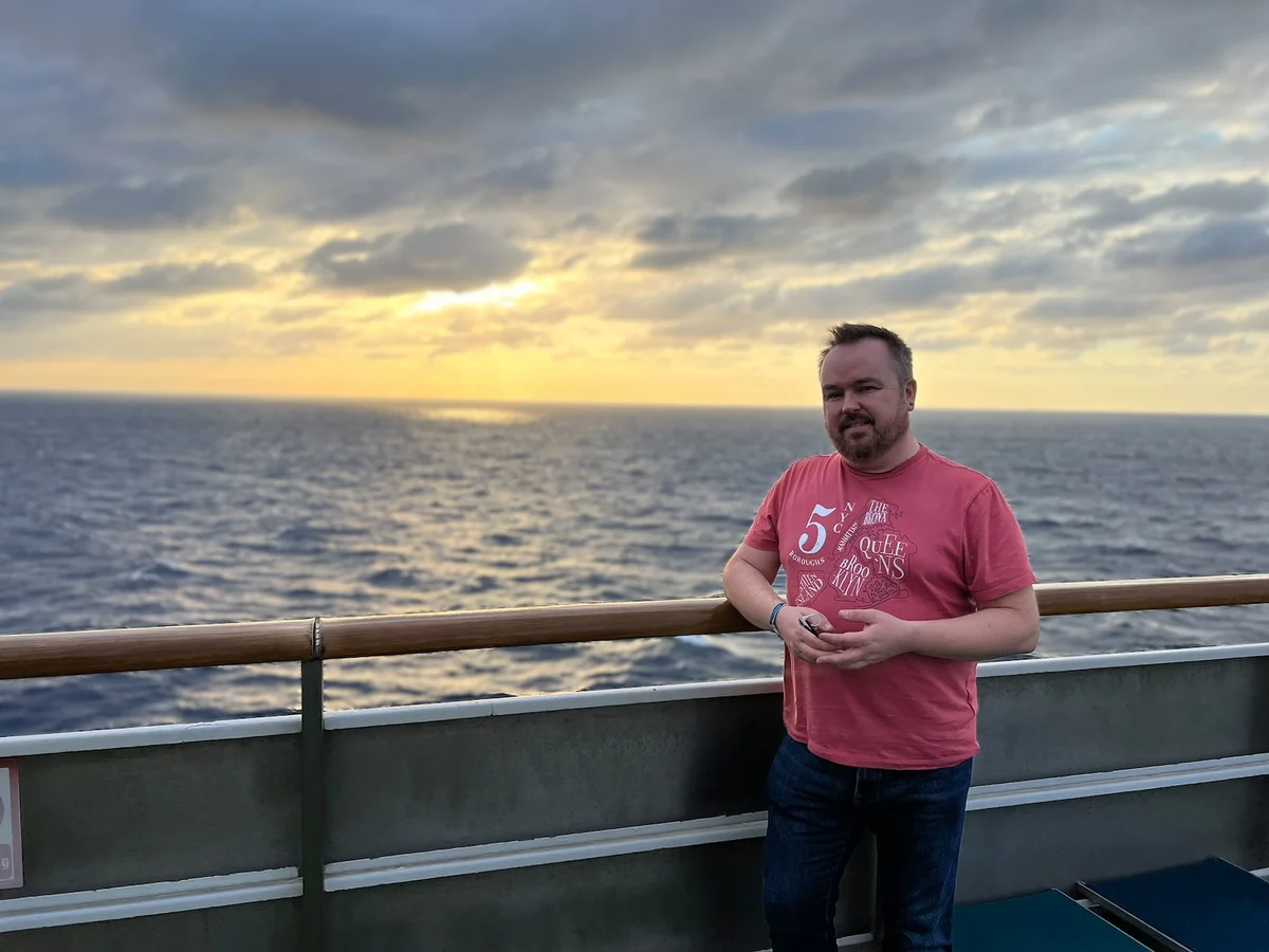 Man standing on deck of Margaritaville Paradise cruise ship at sunset over the ocean