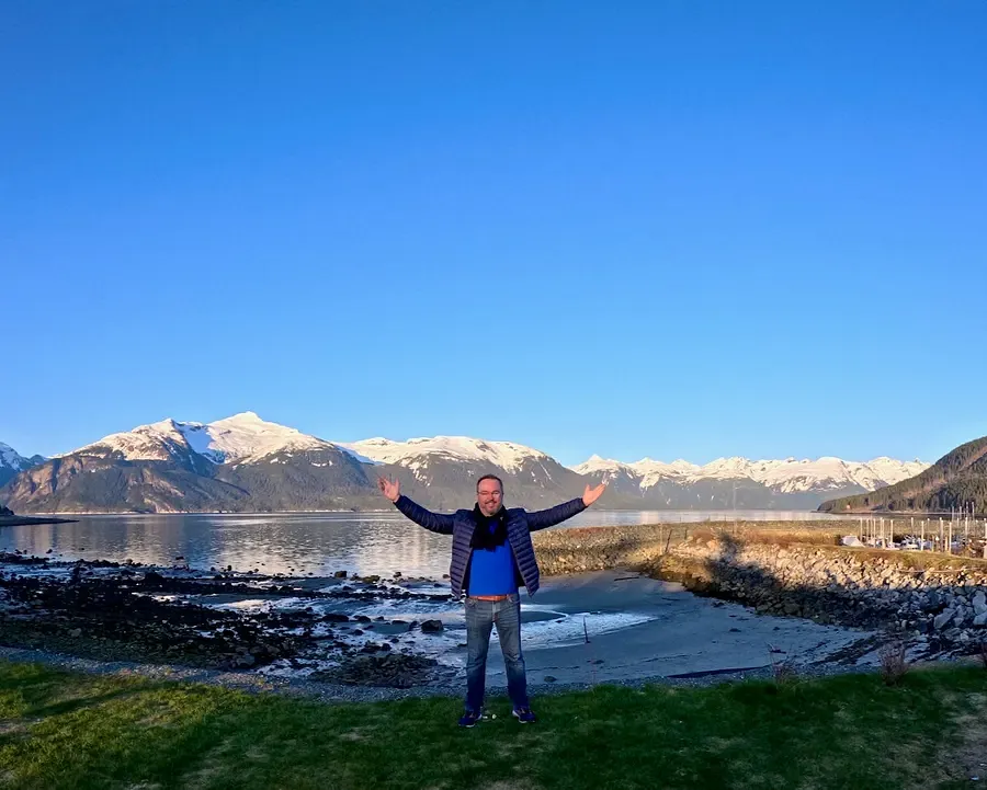 Patrick Hughes with his arms aloft with a backdrop of Portage Cove, Alaska.