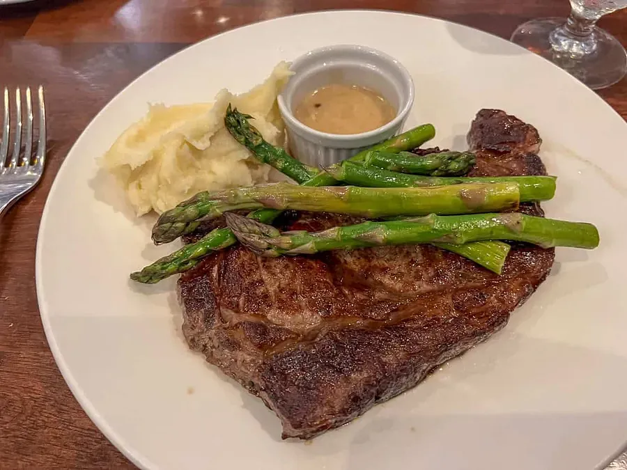 A white plate with a steak heaped with asparagus 