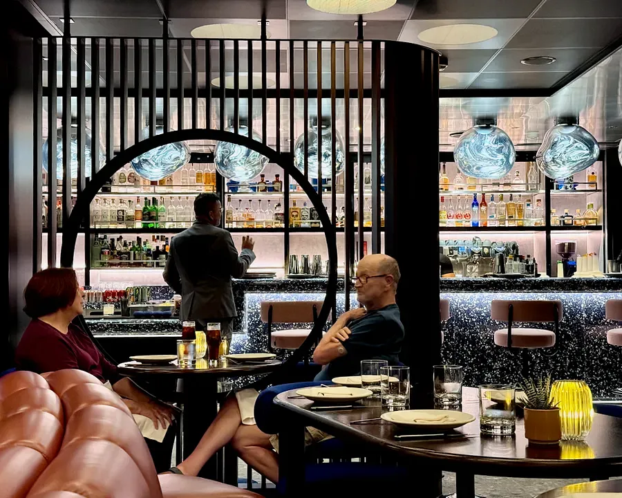 The bar at Pink Agave on Virgin Voyages with bright lights and strictly lined-up bottles 