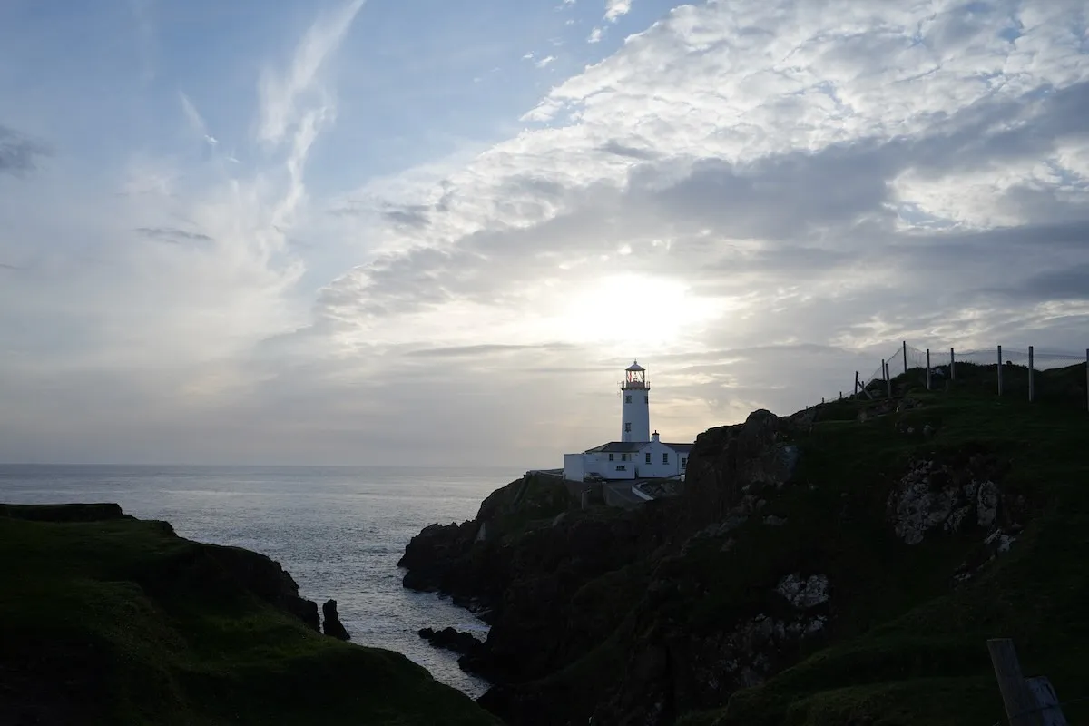 Fanad Head Lighthouse perched on dramatic rocky cliffs overlooking the Atlantic Ocean at dusk