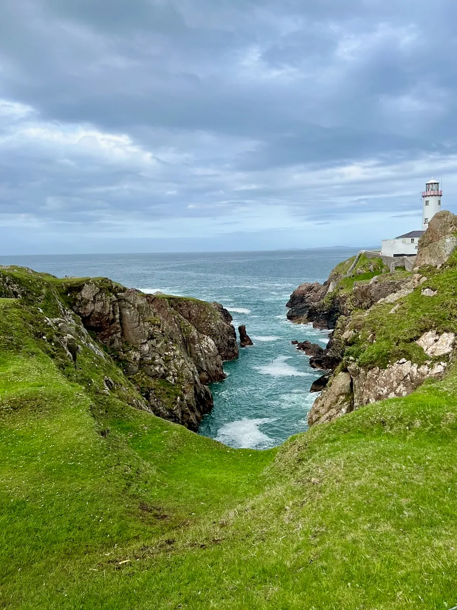 Fanad Head Lighthouse perched on rocky cliffs above turquoise waters and a narrow inlet in Donegal