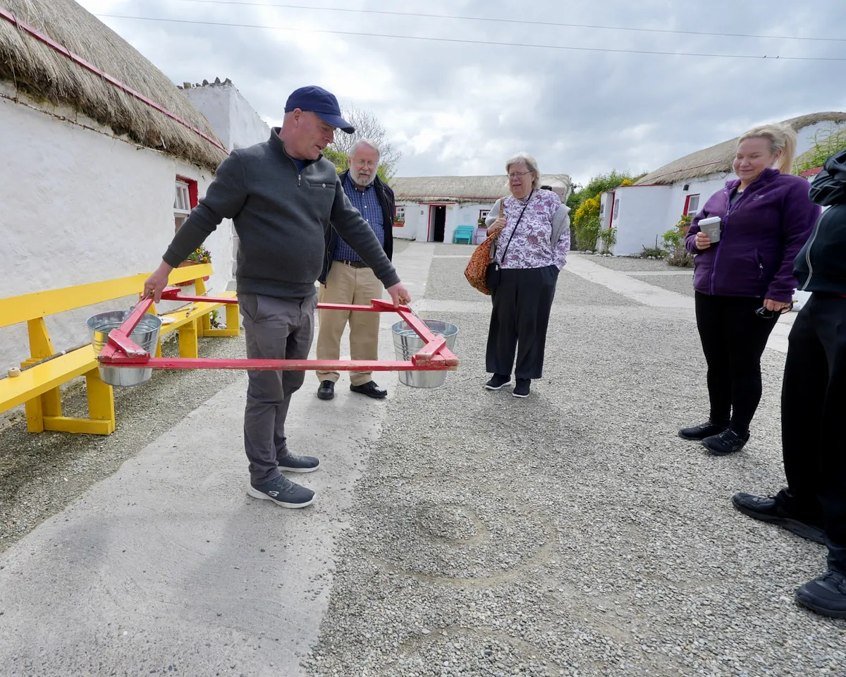 Local guide demonstrating traditional Irish turf-cutting tool at thatched cottage village in Donegal