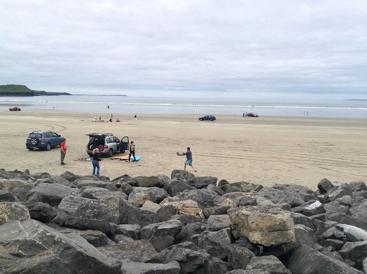 Wide sandy beach at Rossnowlagh with cars parked on sand, families, and rocky breakwater in foreground