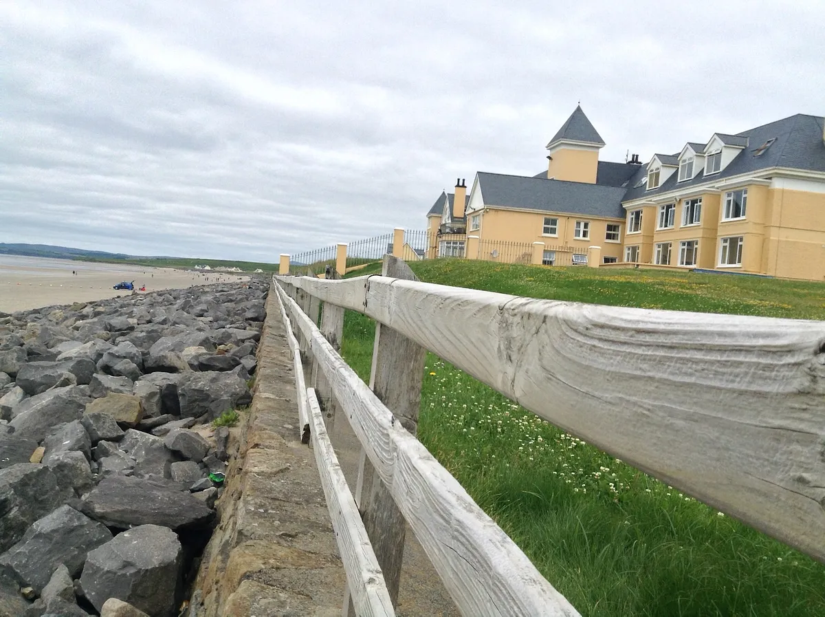 White wooden fence along rocky beach with yellow hotel building in Rossnowlagh