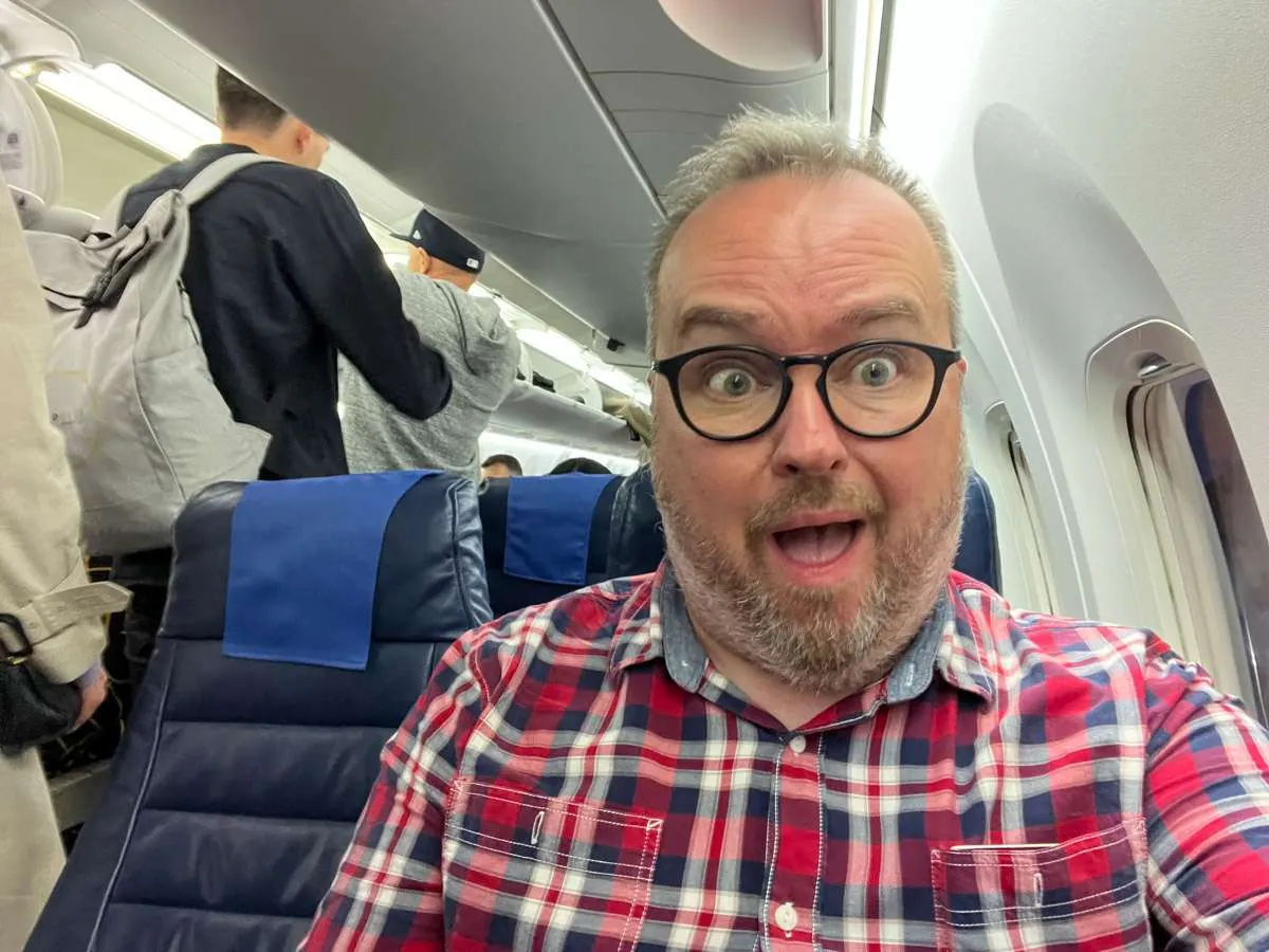 Patrick in an economy seat on a connecting LOT Polish Airlines seat after having paid for business class. 