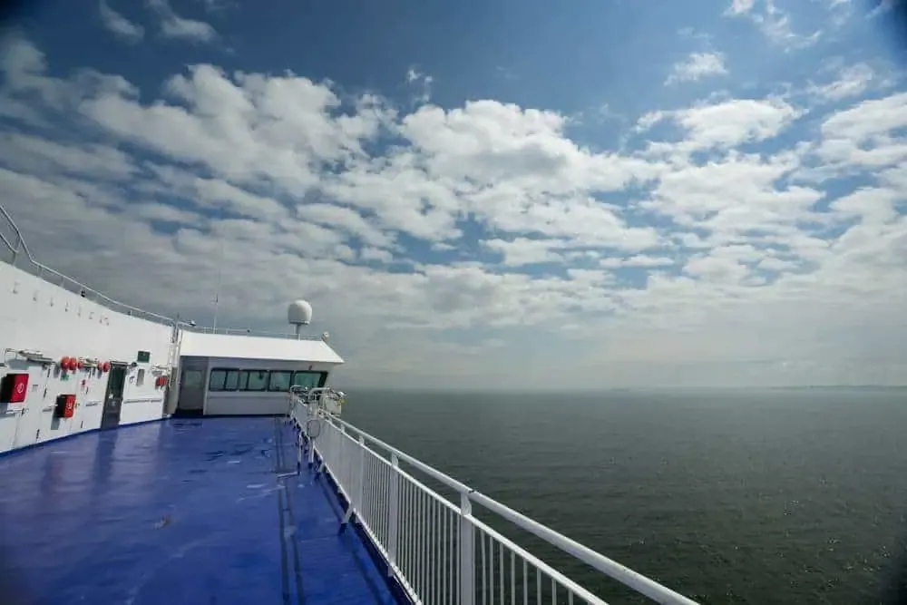 The deck is shown, painted dark blue. The sea is in the background with a bright sky. 
