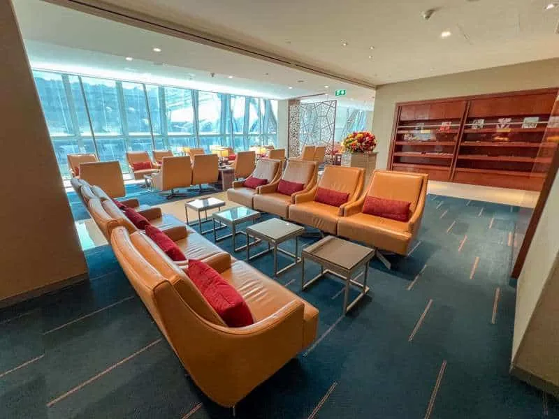 The entrance area at Emirates Business Lounge in Bangkok showing multiple tan-leather seats with red cushions