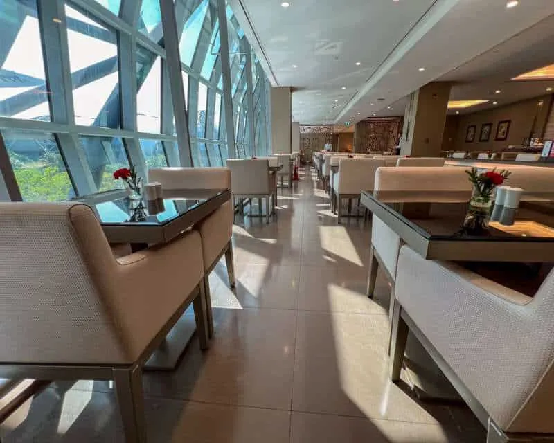 A dining spot at Emirates Bangkok Business Lounge, with light tan chairs and dark wood tables. 
