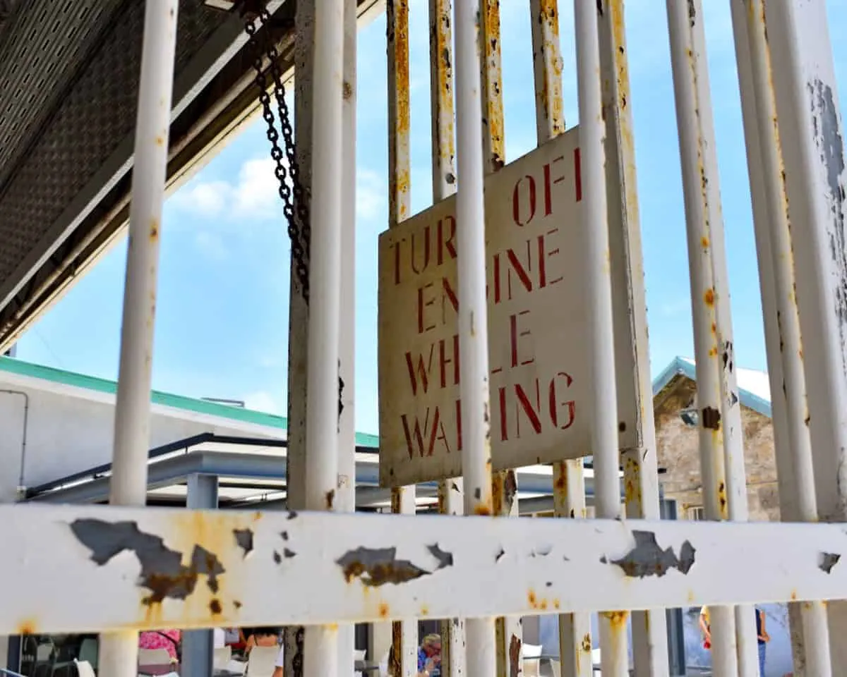 A view of a sign "turn off engine while waiting" through flaking white prison bars at Fremantle Prison