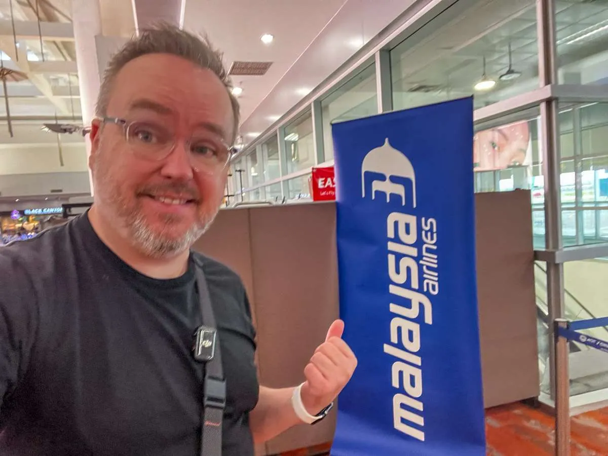 Patrick Hughes standing in front of a Malaysia Airlines sign at Chiang Mai Airport