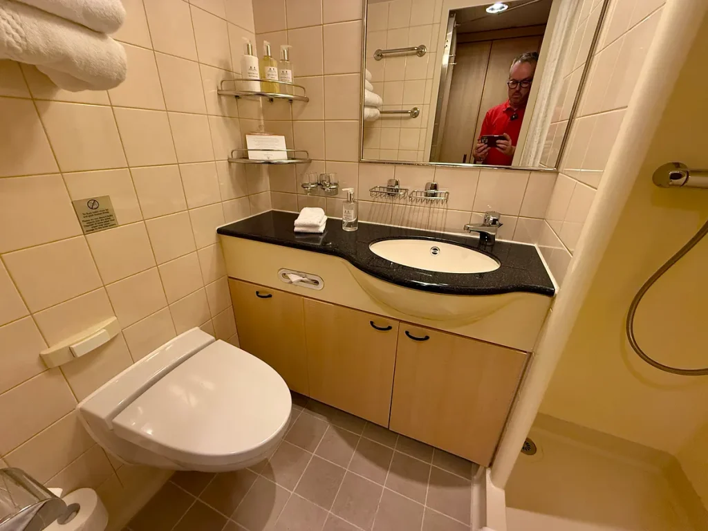 Compact bathroom with beige tile, black granite vanity, and curved wood cabinetry