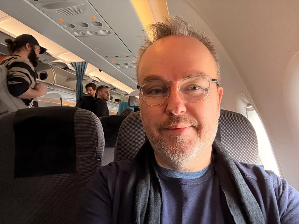 Passenger selfie inside an aircraft cabin with other travelers visible in background seats