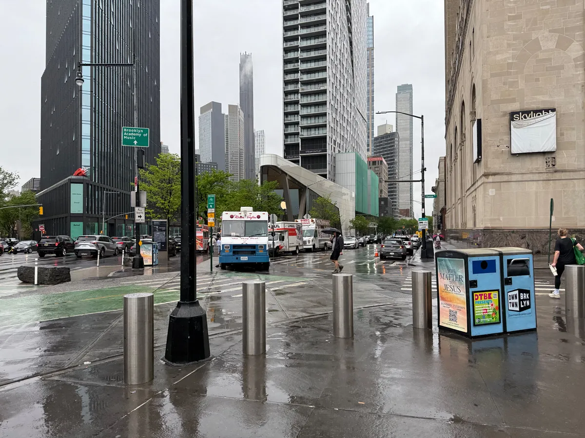 Rainy street corner in downtown Brooklyn with food trucks, high-rise buildings, and wet pavement
