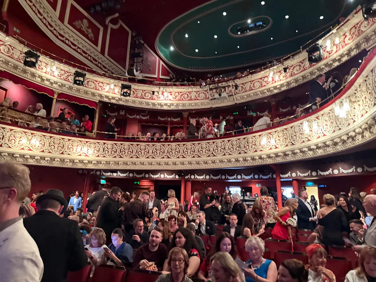 Interior of a West End theatre showing ornate balconies and audience members during intermission