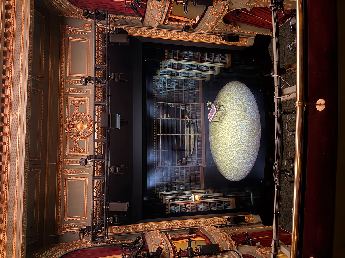 View from upper circle showing ornate gold proscenium arch and stage set at London's West End theatre