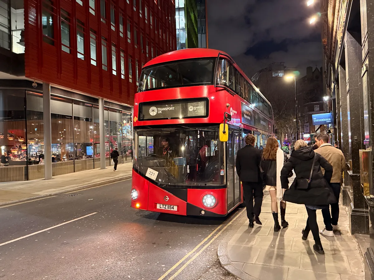 Red double-decker bus on a London street at night with pedestrians boarding