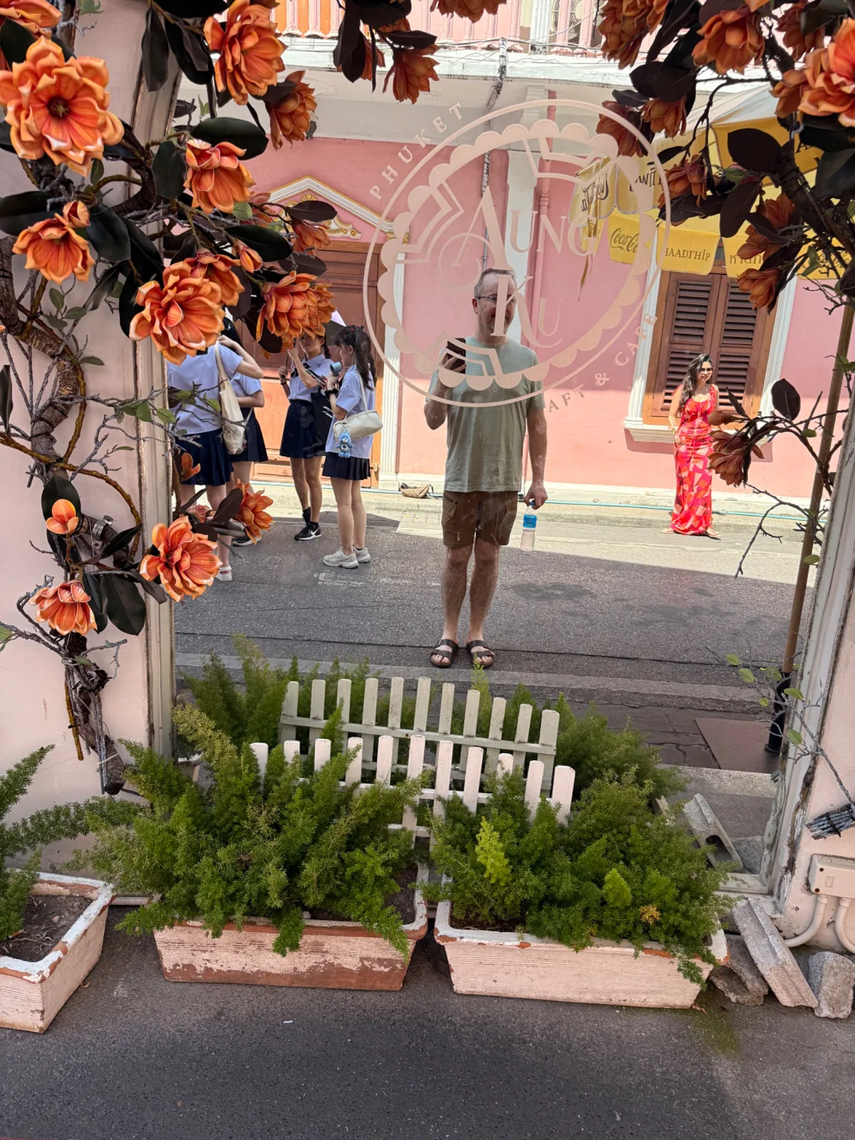 Flower-framed archway entrance to a street in Phuket Old Town with pink cafe building