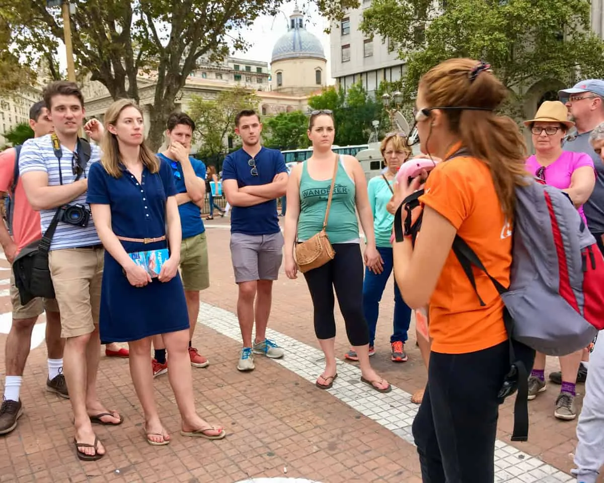 A group of people on a free walking tour in Buenos Aires - the guide is a young woman wearing an orange top and a microphone.