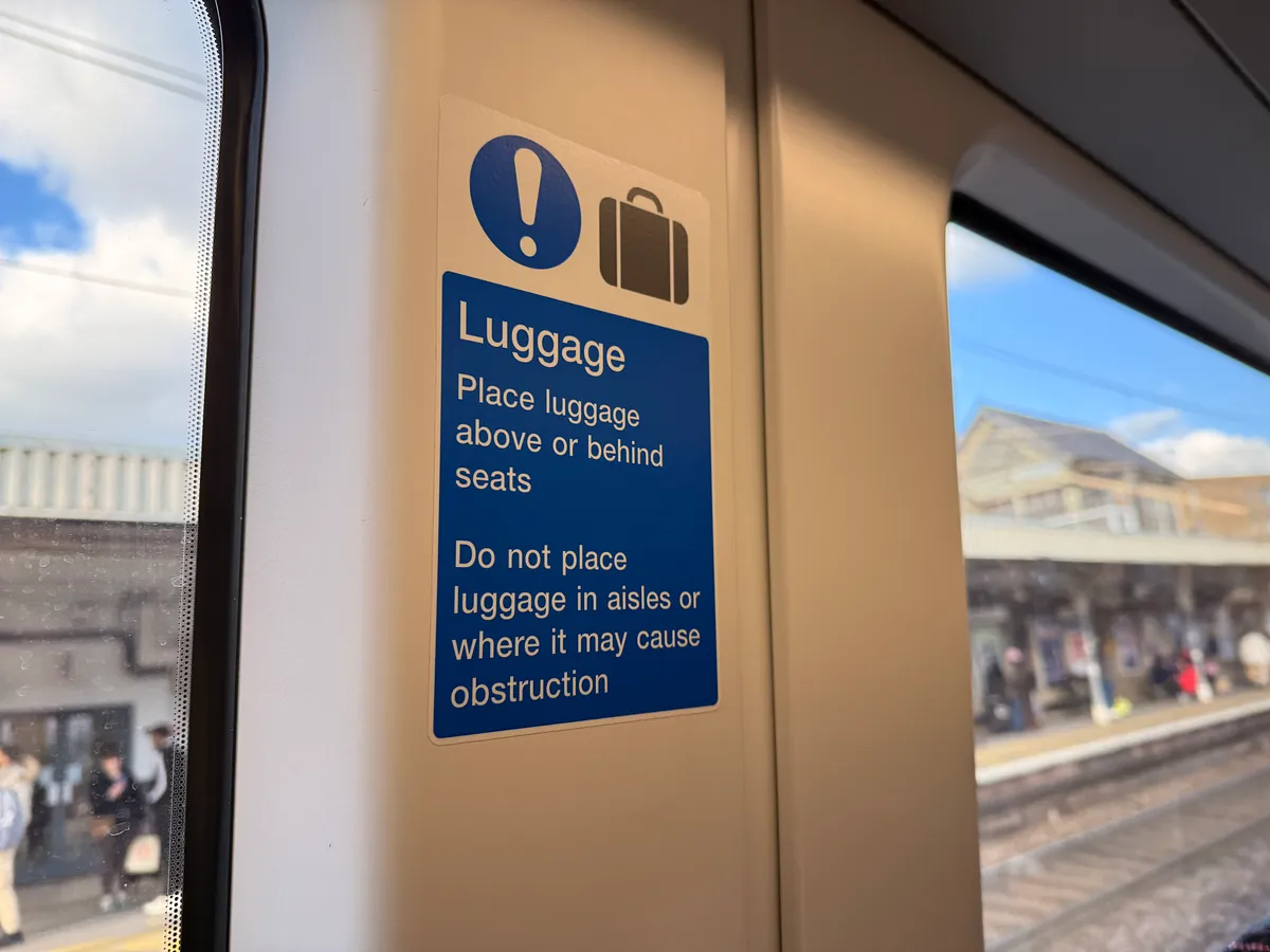 Luggage storage sign on Greater Anglia train interior wall with platform visible through window